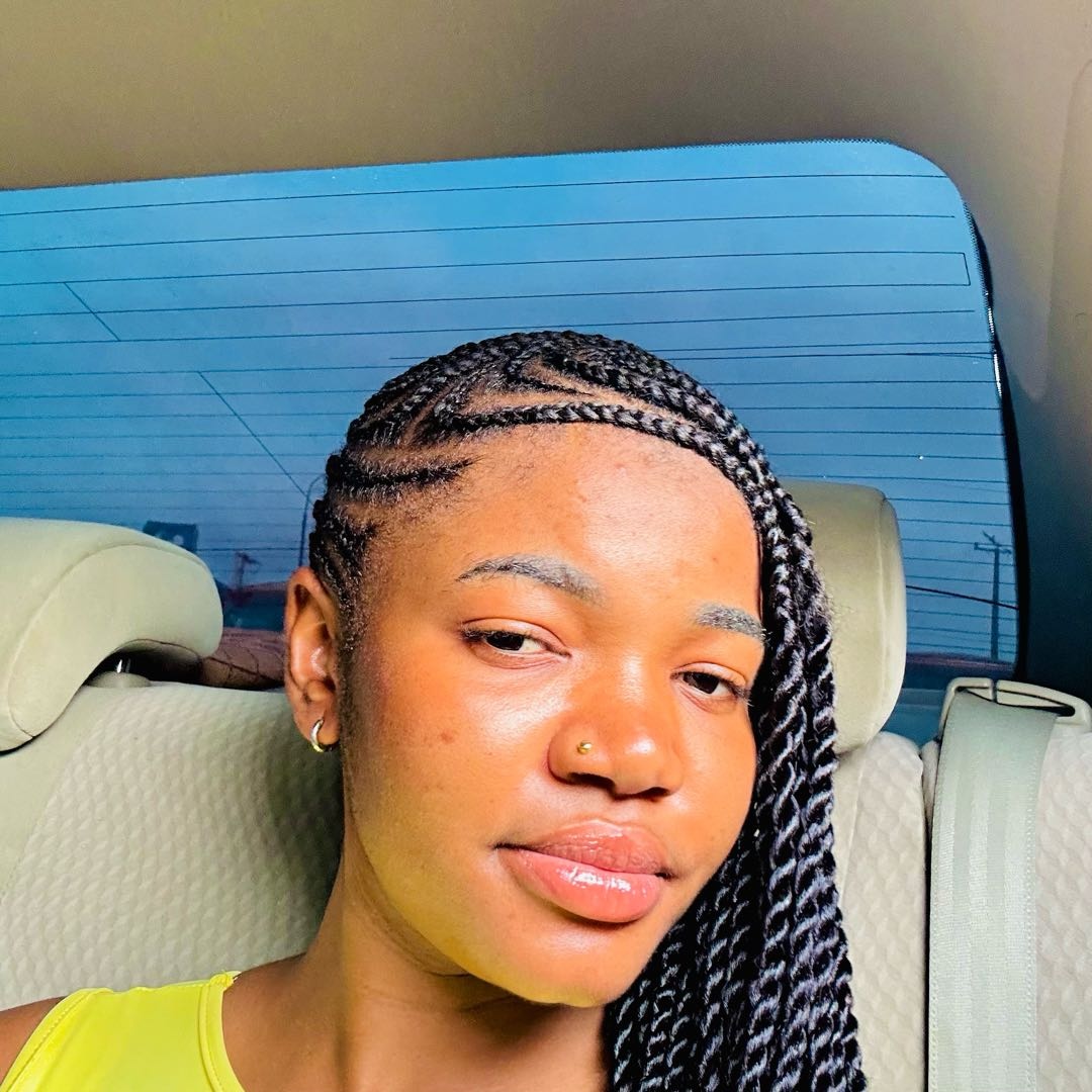 A woman from Nigeria with long braids sitting in a car, calm and relaxed