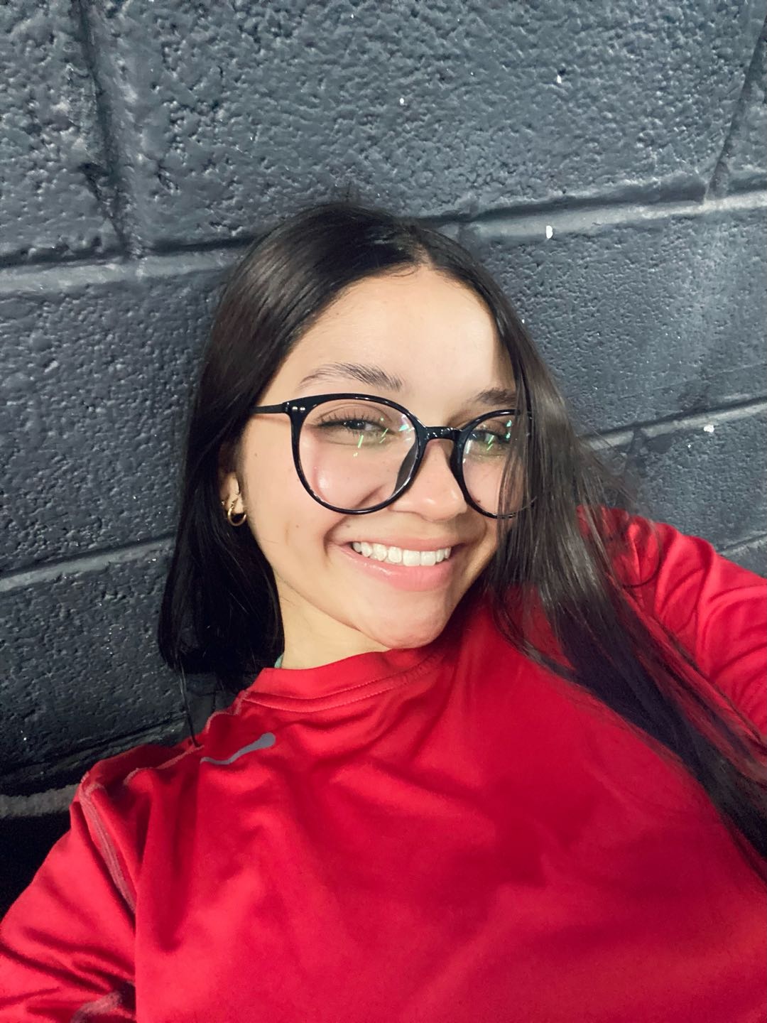 A smiling woman from Venezuela in glasses and a red top, ready for a voice chat with the camera off