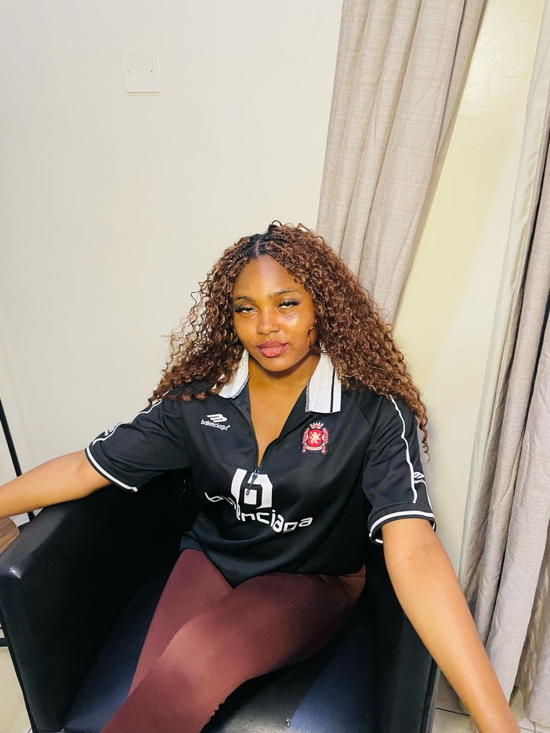 A woman from Nigeria in a football shirt, sitting back as she would in a random cam chat
