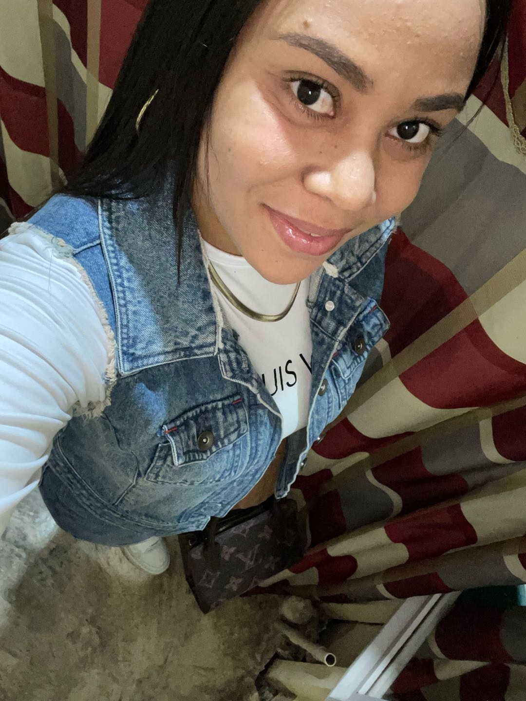 A woman from the Dominican Republic in a denim jacket, smiling at her phone during a text chat