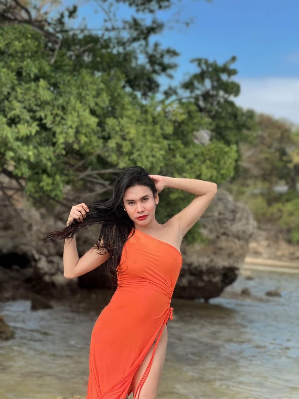 A woman from the Philippines in an orange dress on a rocky beach